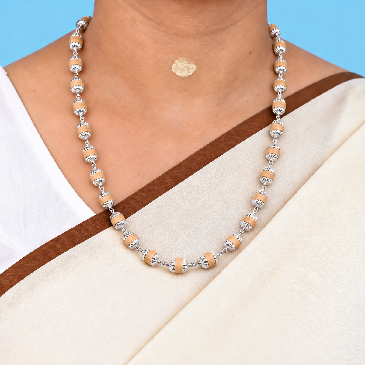 Tulsi mala with light wooden beads and silver-tone petal caps worn by a model in a cream saree against a blue background.