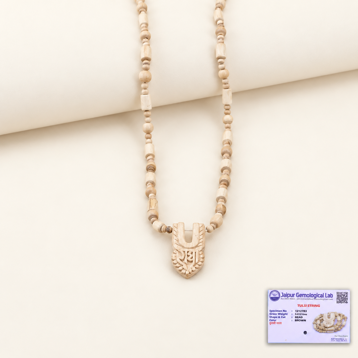Tulsi wood bead mala with a carved pendant on an off-white background, with a certificate at the bottom right.