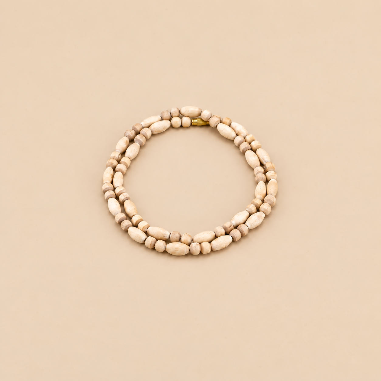 Tulsi wood mala with round and elongated beads arranged in a circle, with a gold-tone clasp on a beige background