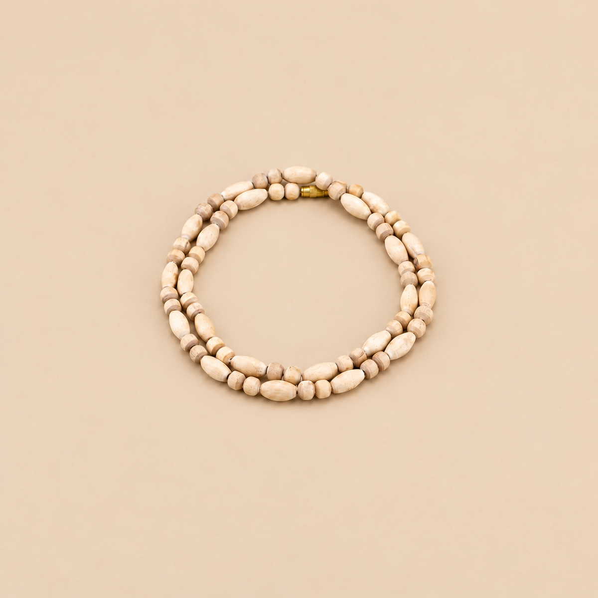 Tulsi wood mala with round and elongated beads arranged in a circle, with a gold-tone clasp on a beige background