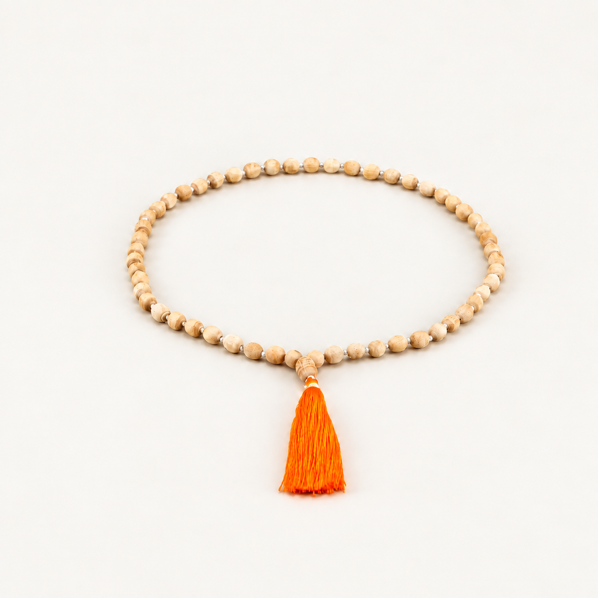 Tulsi wood bead mala with an orange tassel arranged in an oval on an off-white background.