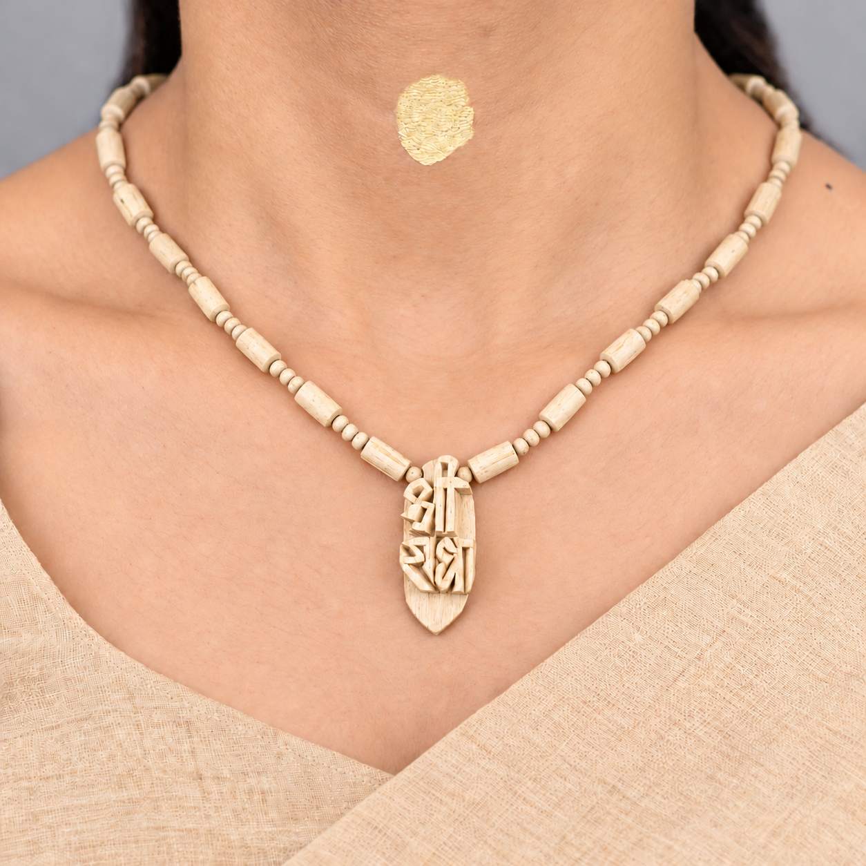 Woman wearing a natural Tulsi wood mala with cylindrical beads and carved wooden pendant over a beige outfit.