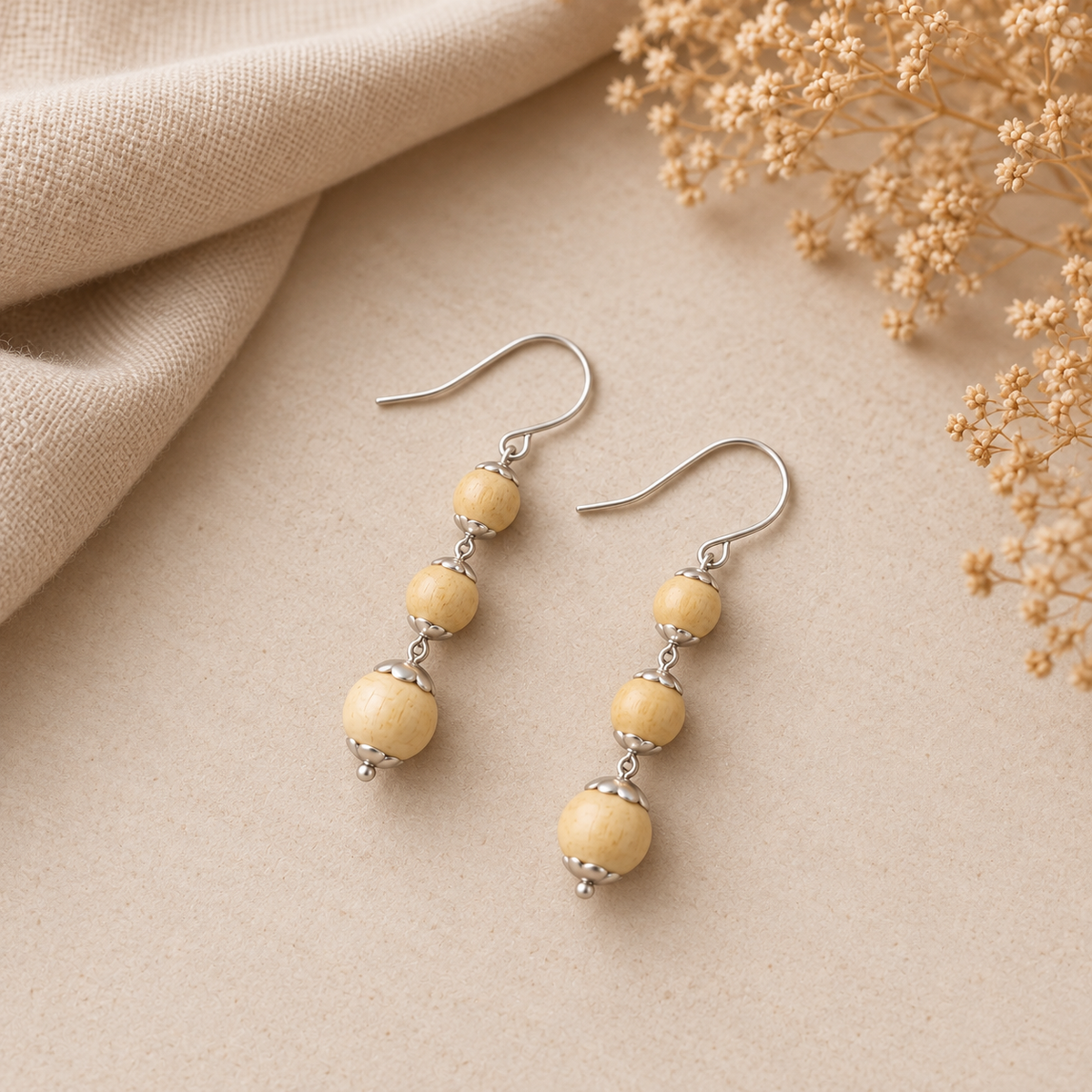 Pair of three-bead Tulsi wood drop earrings with silver-toned hooks resting on a warm off-white surface.