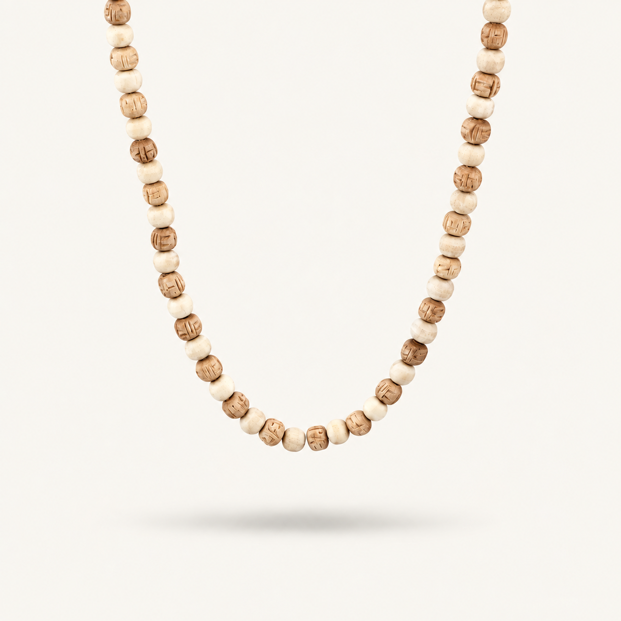 Close-up of a Tulsi mala with alternating light and carved brown beads on an off-white background.