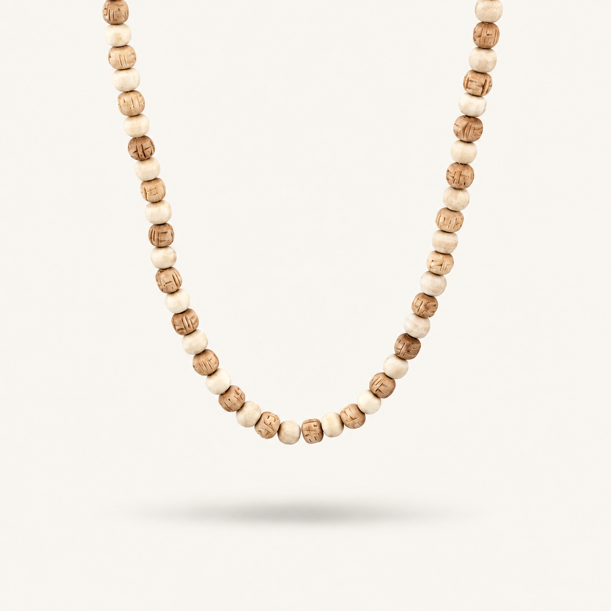 Close-up of a Tulsi mala with alternating light and carved brown beads on an off-white background.