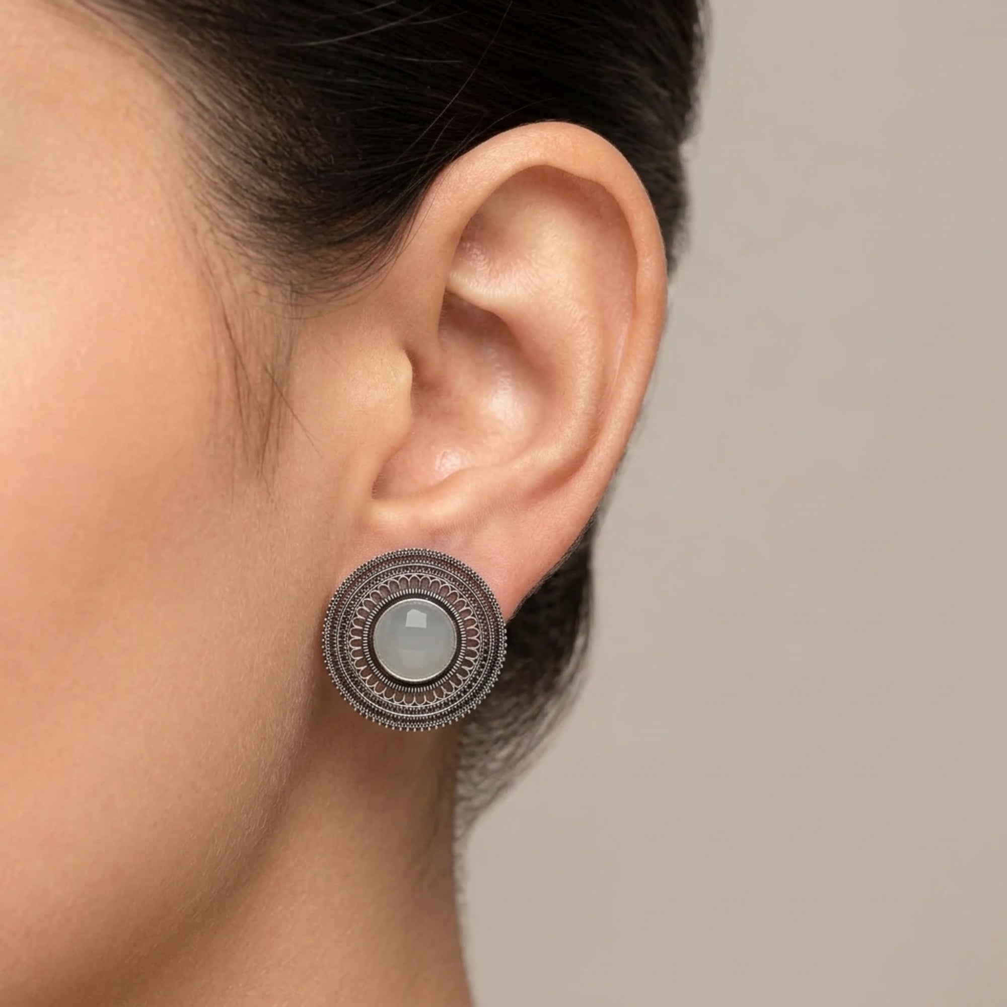 White oxidized metal stud earring with round stone and detailed filigree design worn on ear